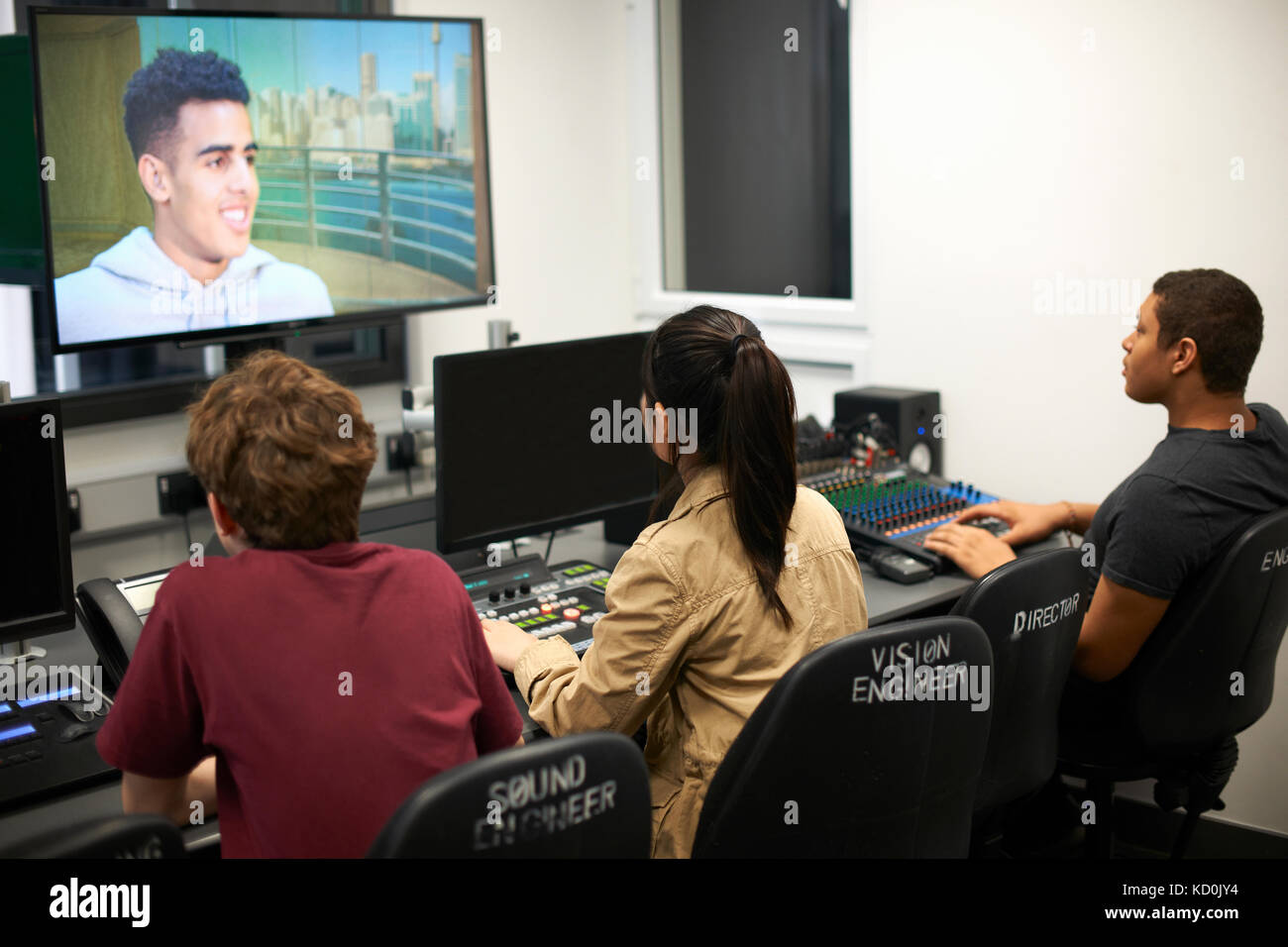 Young male and female college students at mixing desk watching TV screen Stock Photo
