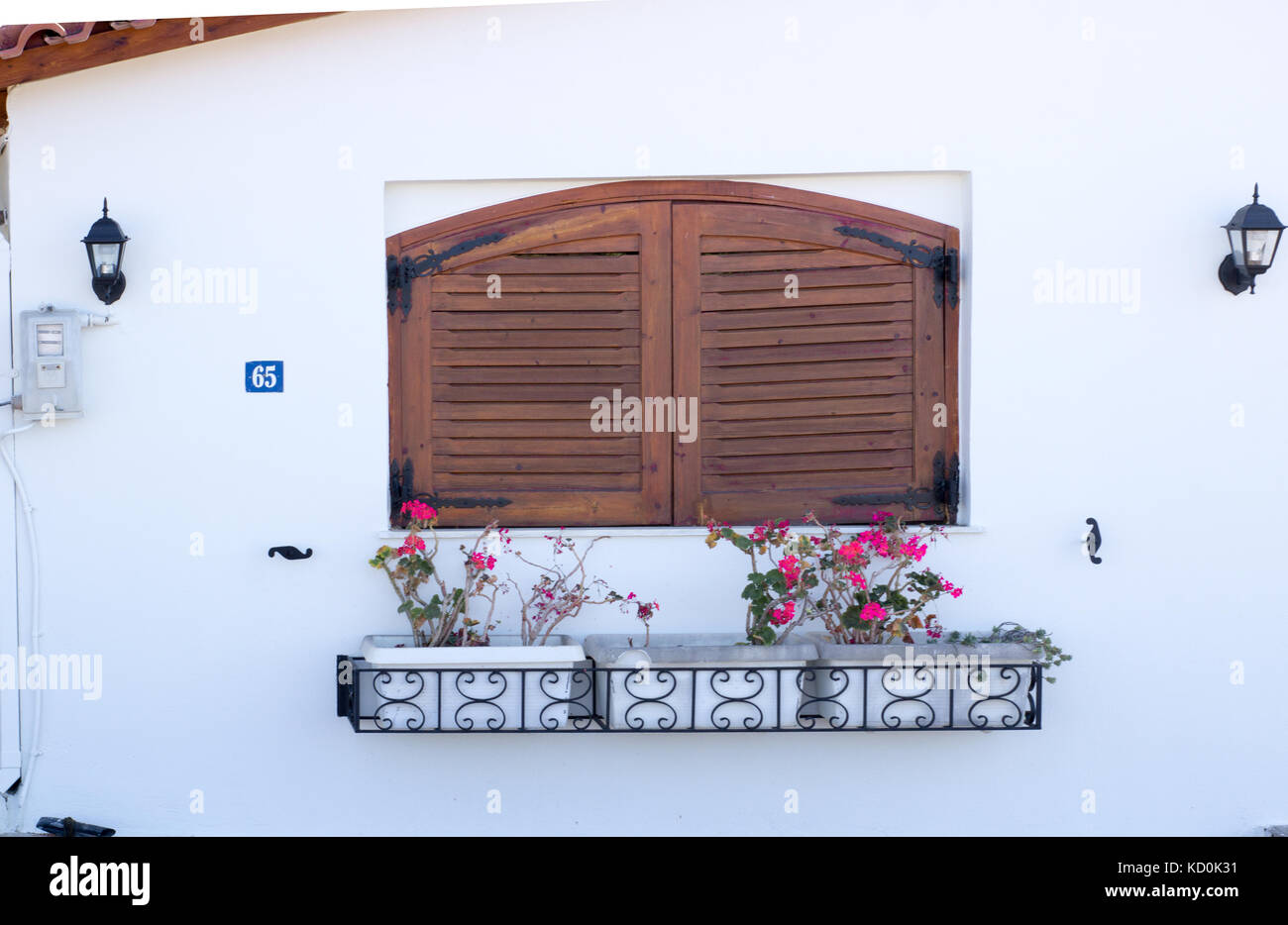 the exterior of a small beautiful house with a window with closed shutters and flowers Stock Photo
