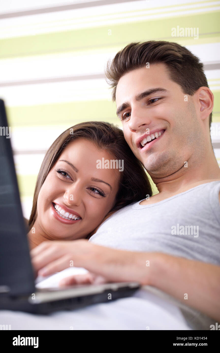 Smiling couple using a laptop lying on their bed at home Stock Photo ...