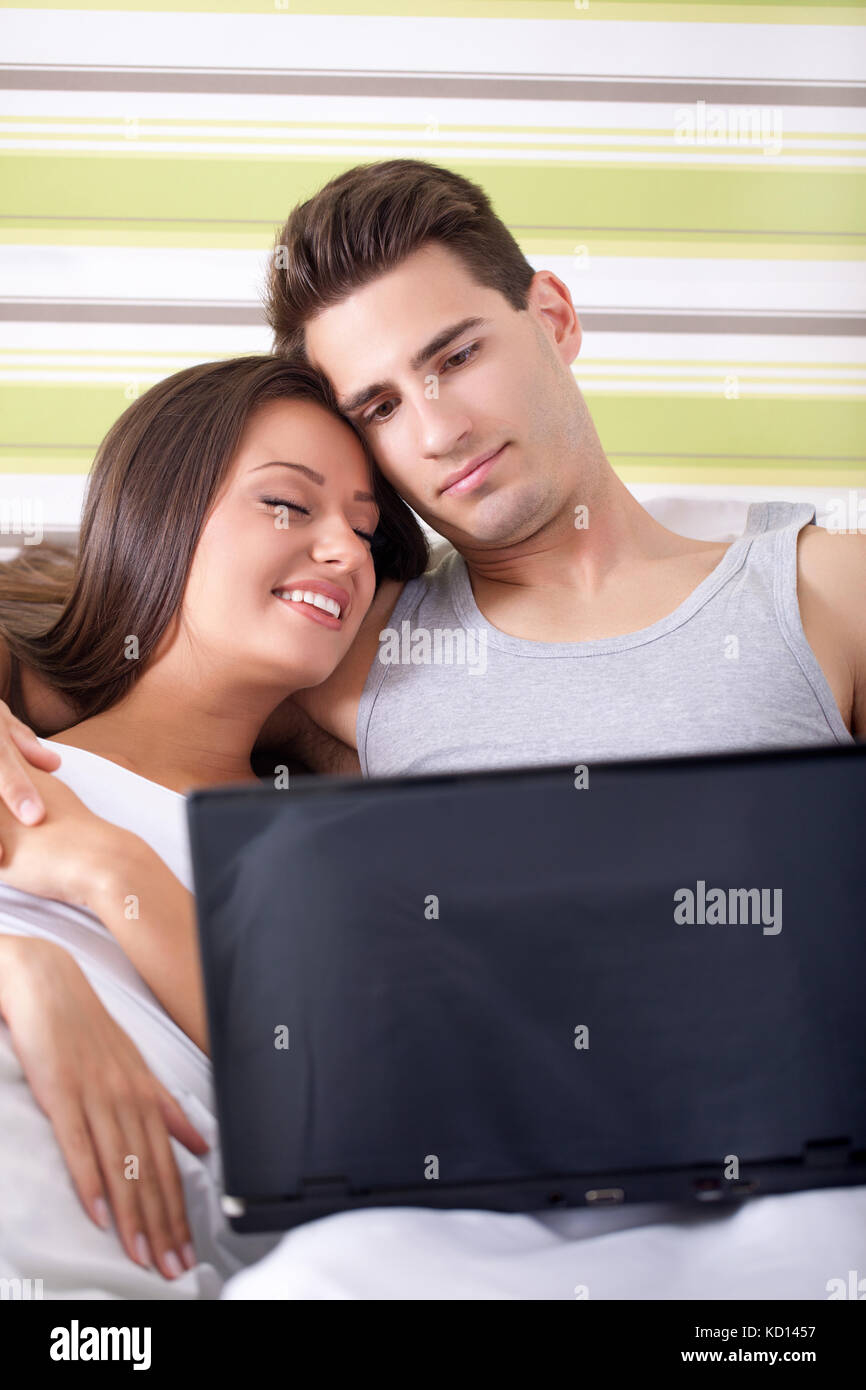 Couple lying in bed with laptop smiling and enjoying Stock Photo - Alamy