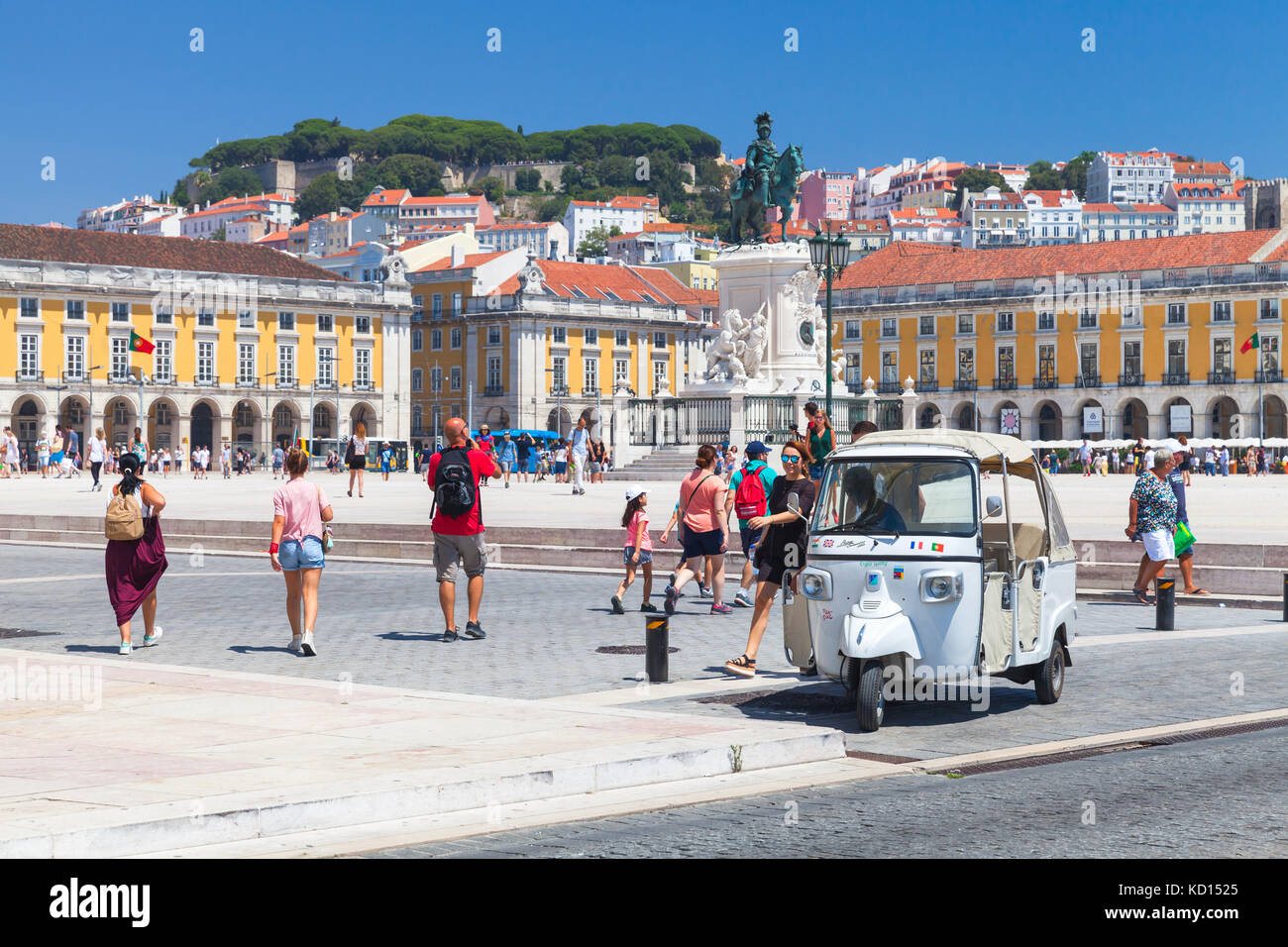Lisbon, Portugal - August 12, 2017: White Tuk Tuk taxi cab stands on Commerce Square in Lisbon. Ordinary people and tourists walk nearby Stock Photo