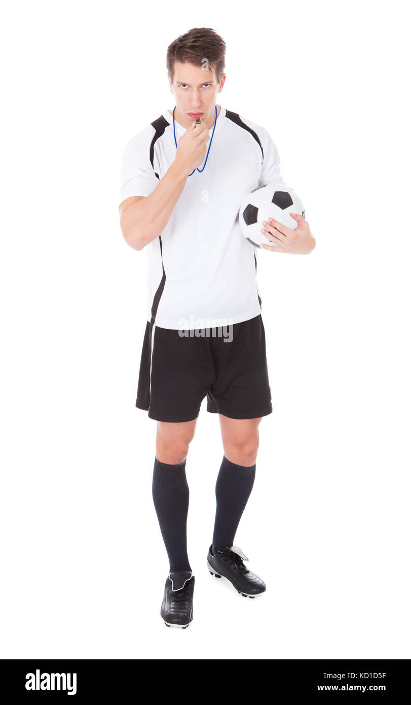 Portrait Of Young Male Soccer Referee Holding Football And Blowing Whistle Stock Photo