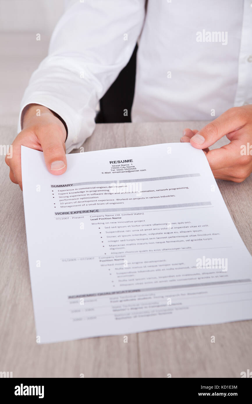 Close-up Of Businessman's Hand Holding Resume On Desk Stock Photo