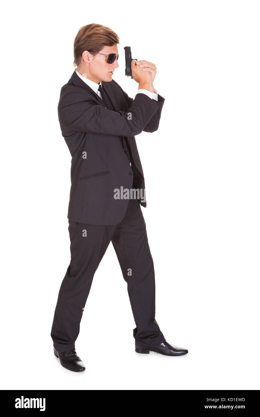 Young Man In Black Suit Holding A Gun On White Background Stock Photo