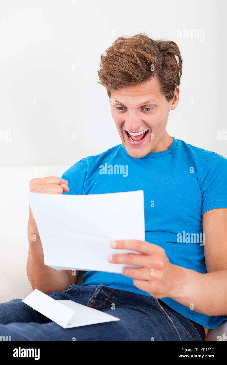 Excited Young Man Clenching His Fist Looking At Paper Stock Photo