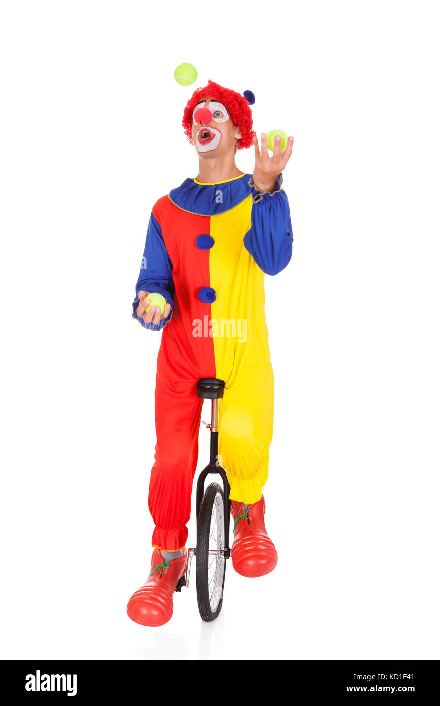 Portrait Of A Clown Juggling With Balls On Unicycle Over White Background Stock Photo