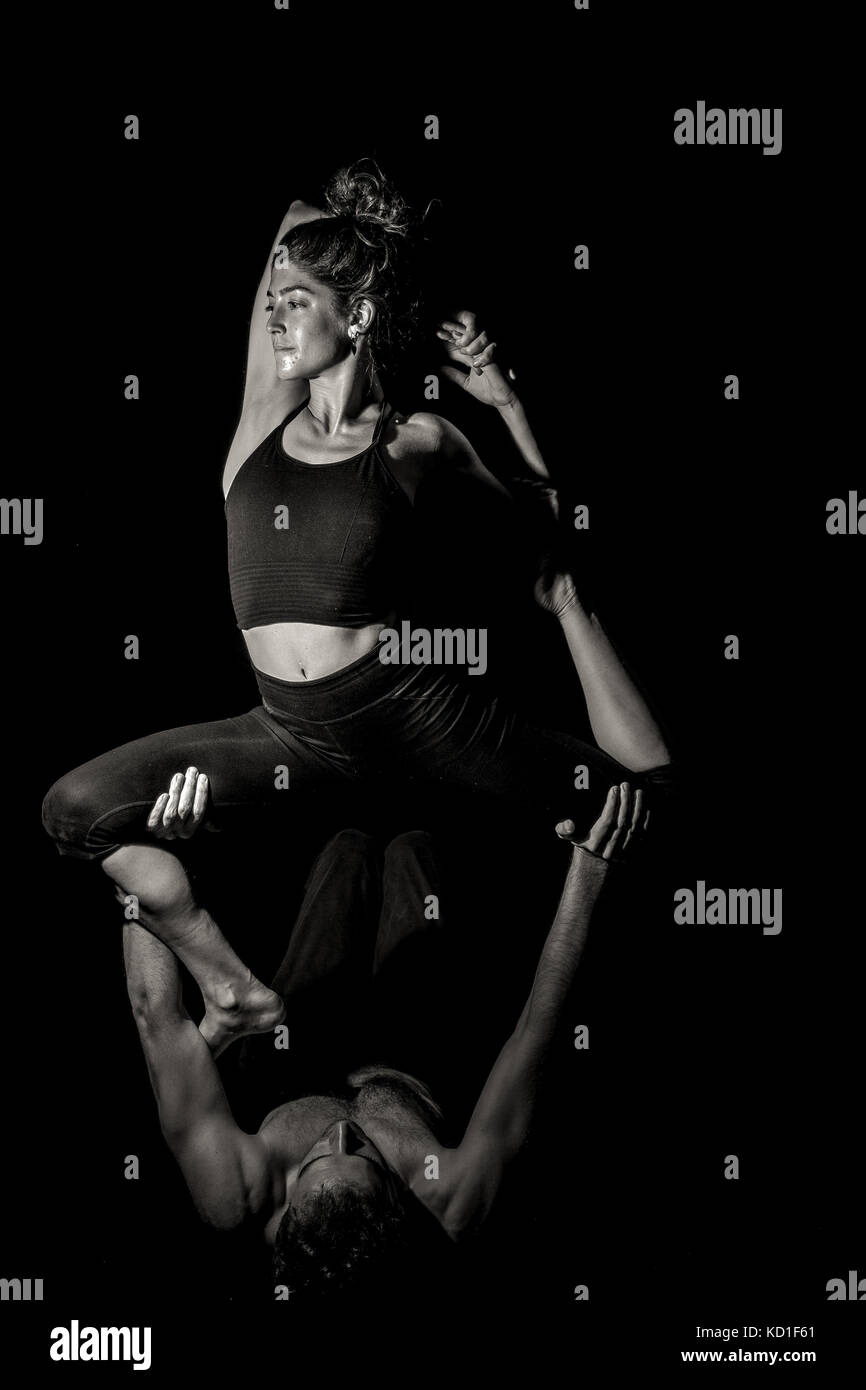 Couple in acroyoga position on black background with single light in black and white Stock Photo