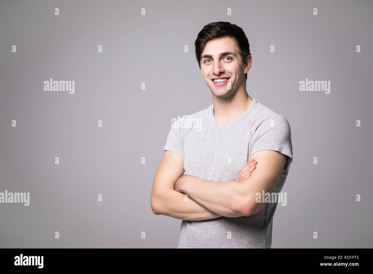 Portrait of a happy casual man standing with arms folded over gray ...