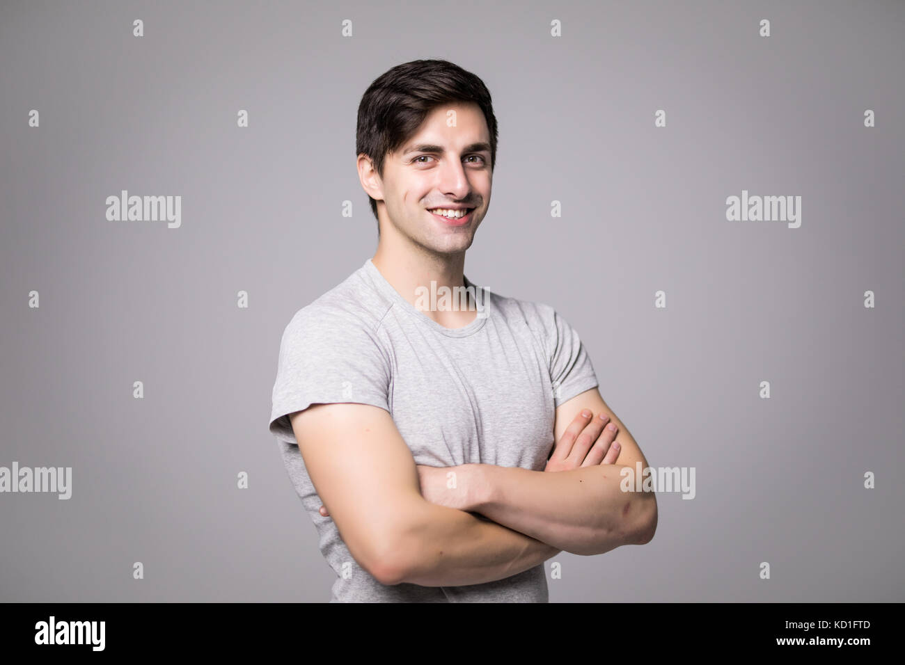 Portrait of a happy casual man standing with arms folded over gray ...