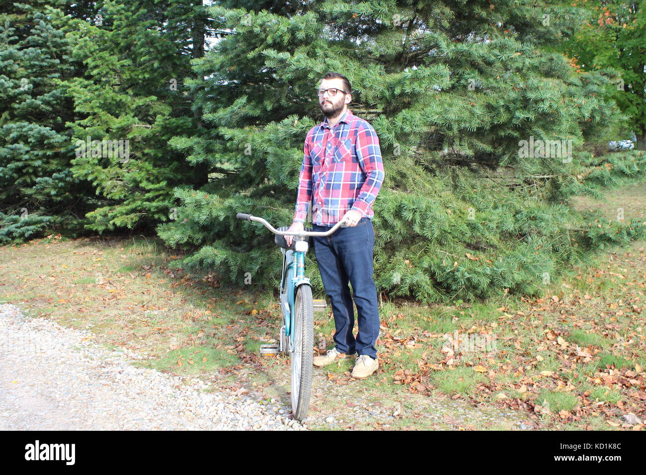 A man and model wearing a flannel plaid shirt with blue jeans rides and poses with a vintage bike/bicycle in the country Stock Photo
