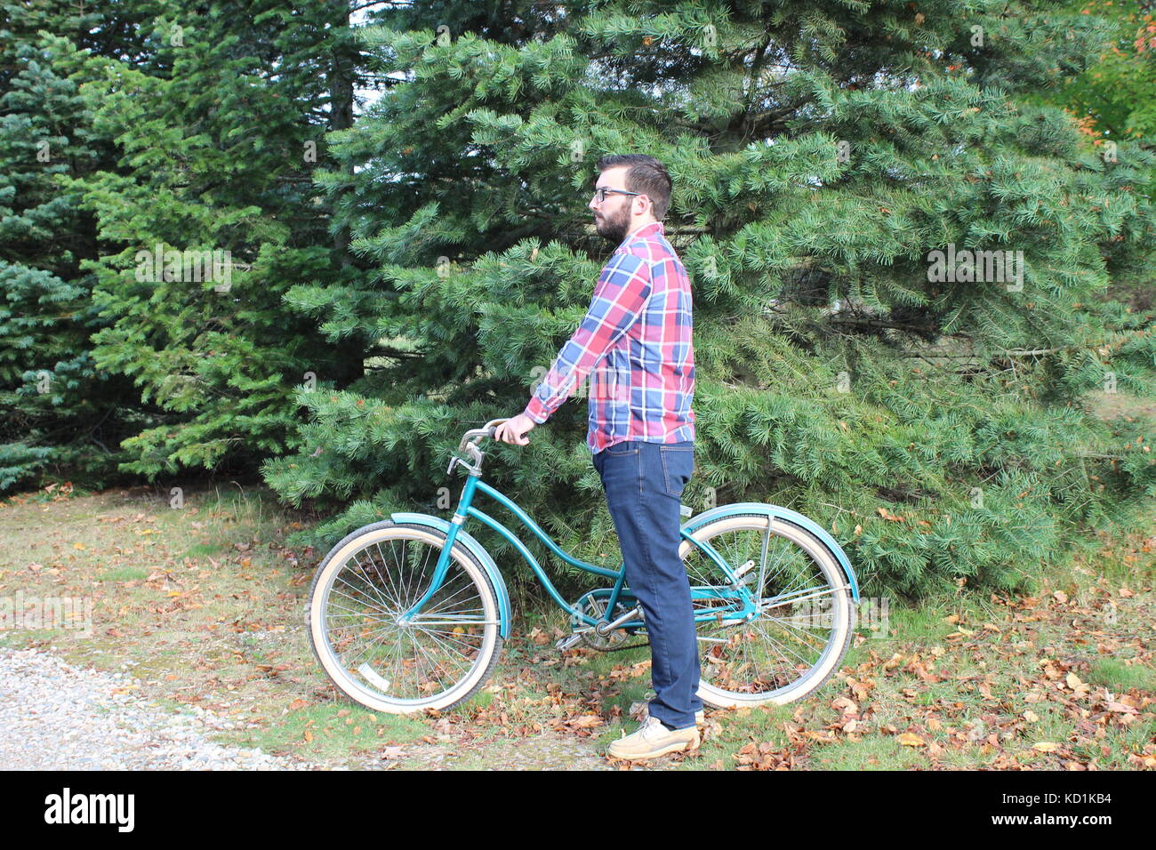 A man and model wearing a flannel plaid shirt with blue jeans rides and poses with a vintage bike/bicycle in the country Stock Photo