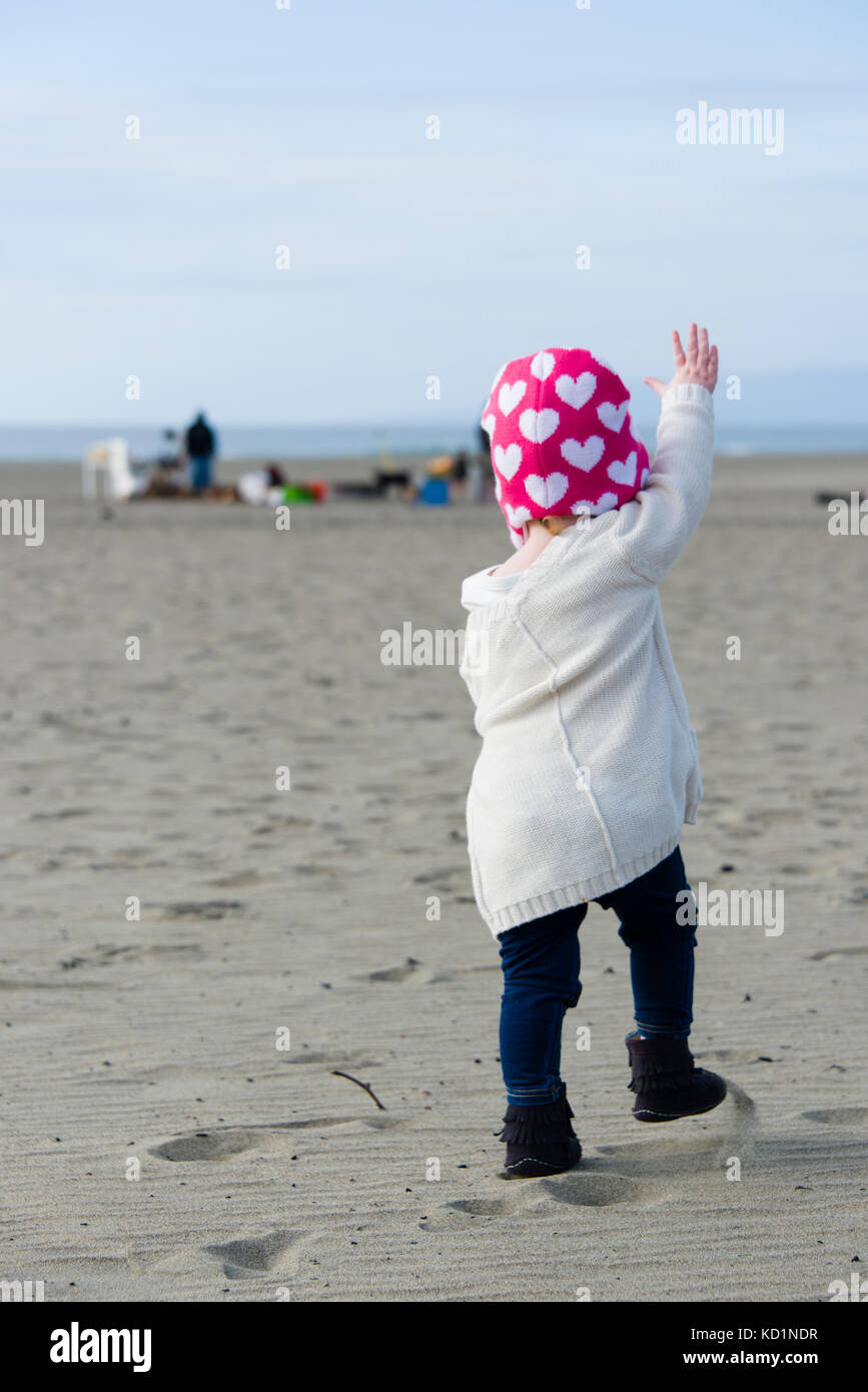 One-year-old girl with raised hand waving to people on the beach. Ocean Beach, San Francisco, California Stock Photo