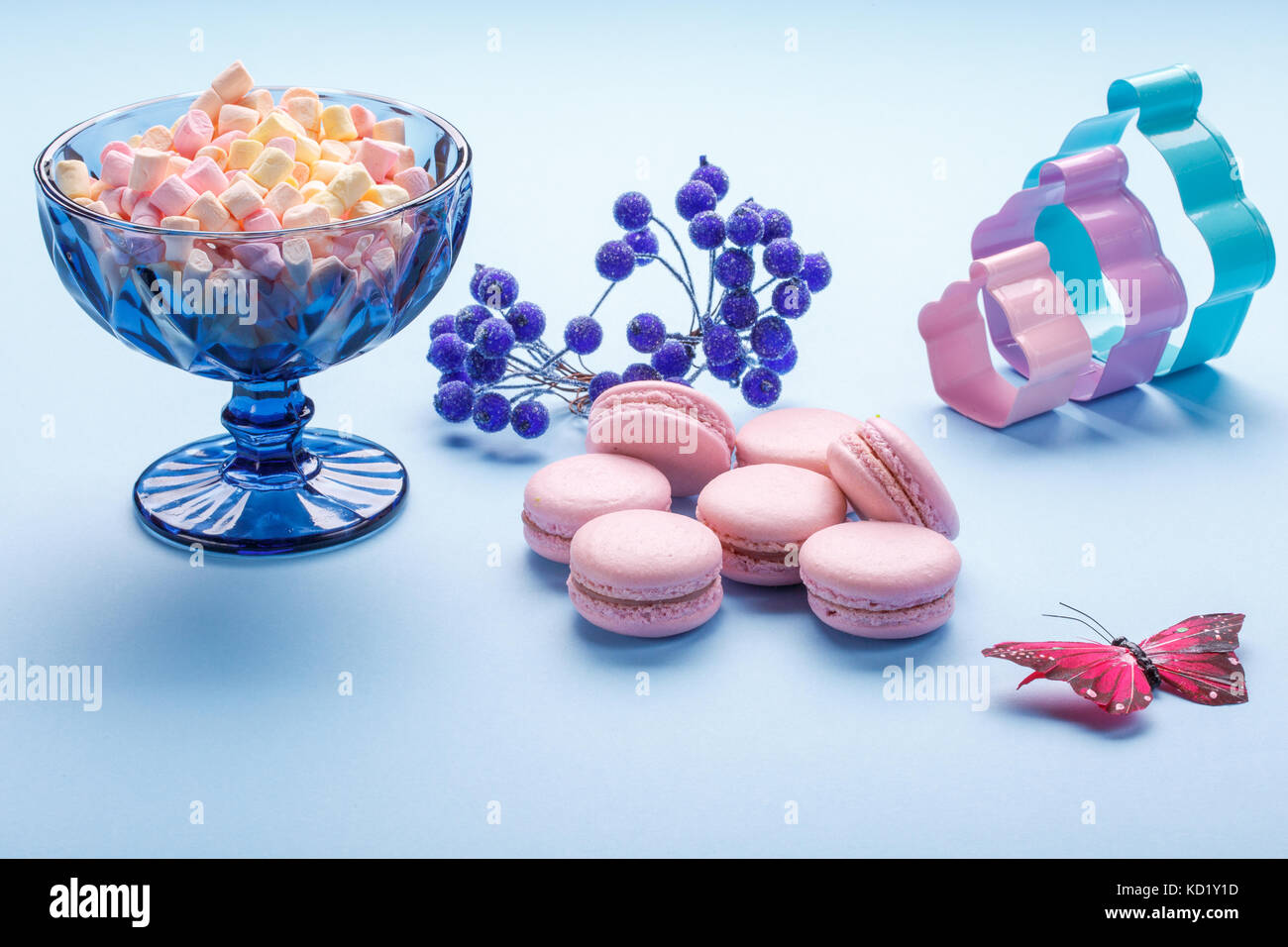 Macaroon cakes with colorful fluffy marshmallows in blue vase over blue background. Stock Photo