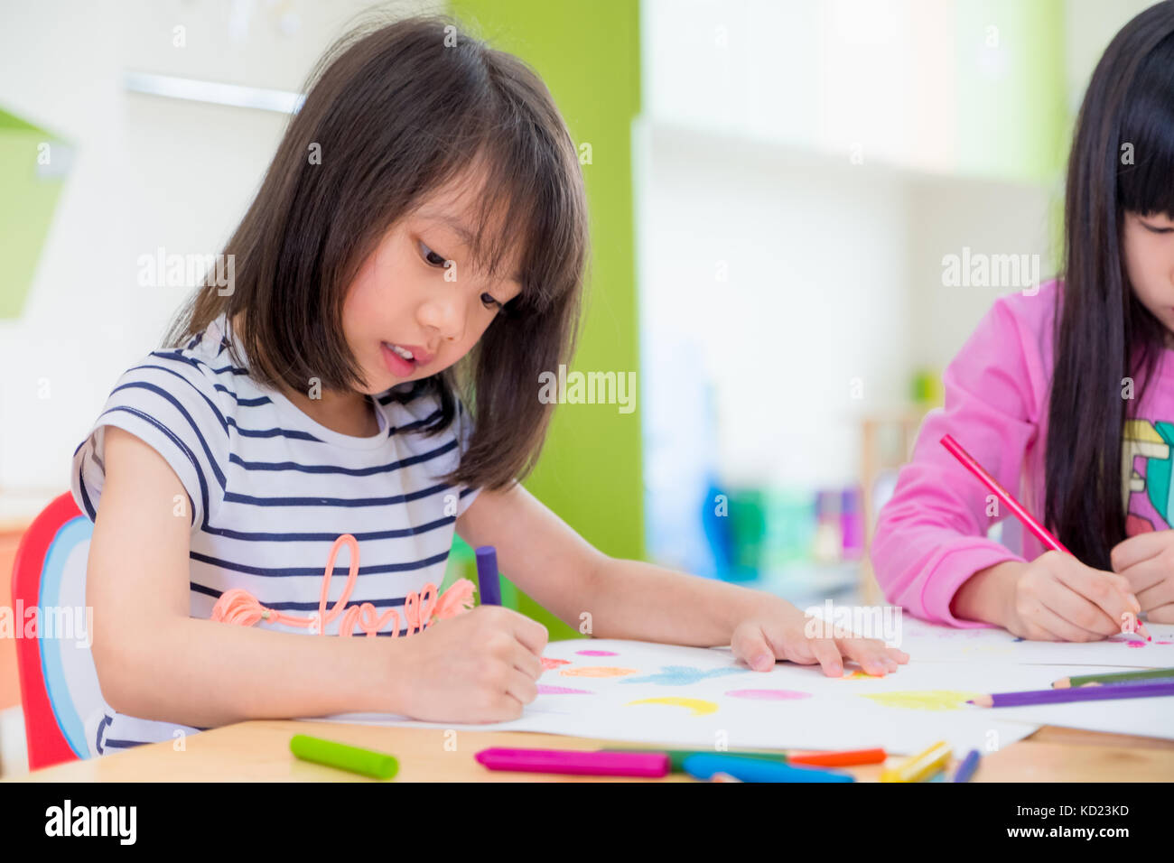 Preschool girl kid drawing with color pencil on white paper on table in classroom with friends and teacher,Kindergarten education concept Stock Photo