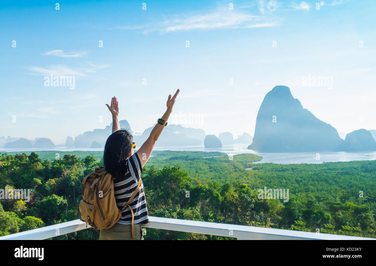 Happy young traveler woman backpacker raised arm up to sky enjoying a beautiful of nature at mountain panorama view point and sea,Freedom wanderlust,K Stock Photo