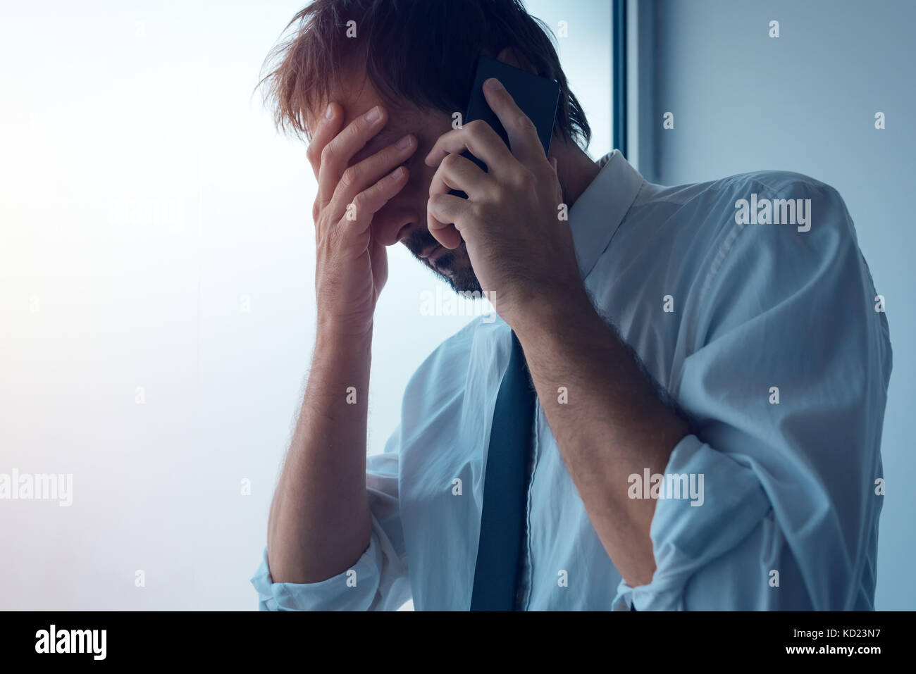 Businessman standing next to office window and using smartphone. Business communication over sms messages or mobile apps. Business person received bad Stock Photo