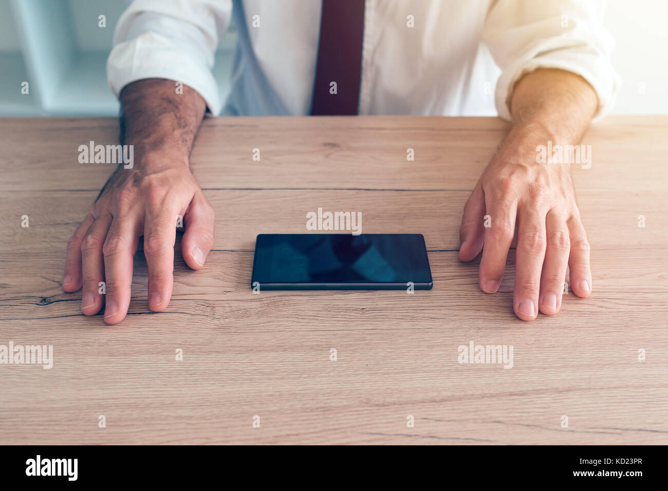 Businessman fighting mobile phone addiction crisis. Business person making effort to resist using smartphone device on office desk. Stock Photo