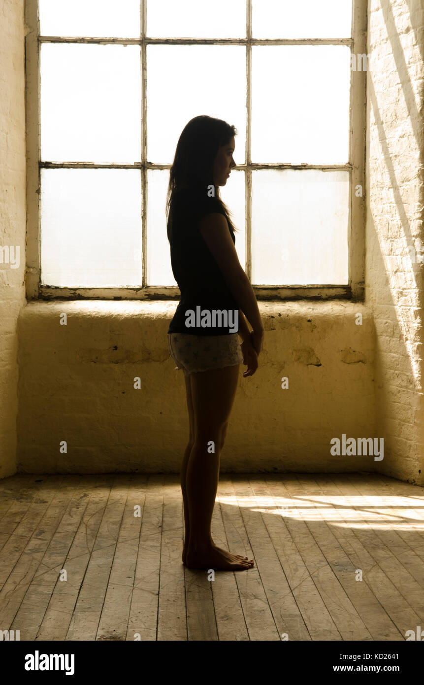 Side view silhouette of a teenage girl standing by the window Stock Photo