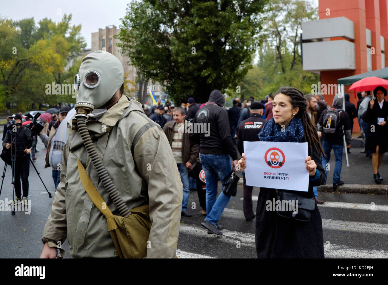 Kryvyi Rih, Ukraine - October 9, 2017: Man wearing gas masks and young woman holding poster 'Stop to poison Kryvyi Rih' near ArcelorMittal Kryvyi Rih PJSC brand monument during anti-pollution protest meeting Credit: Dmytro Aliokhin/Alamy Live News Stock Photo