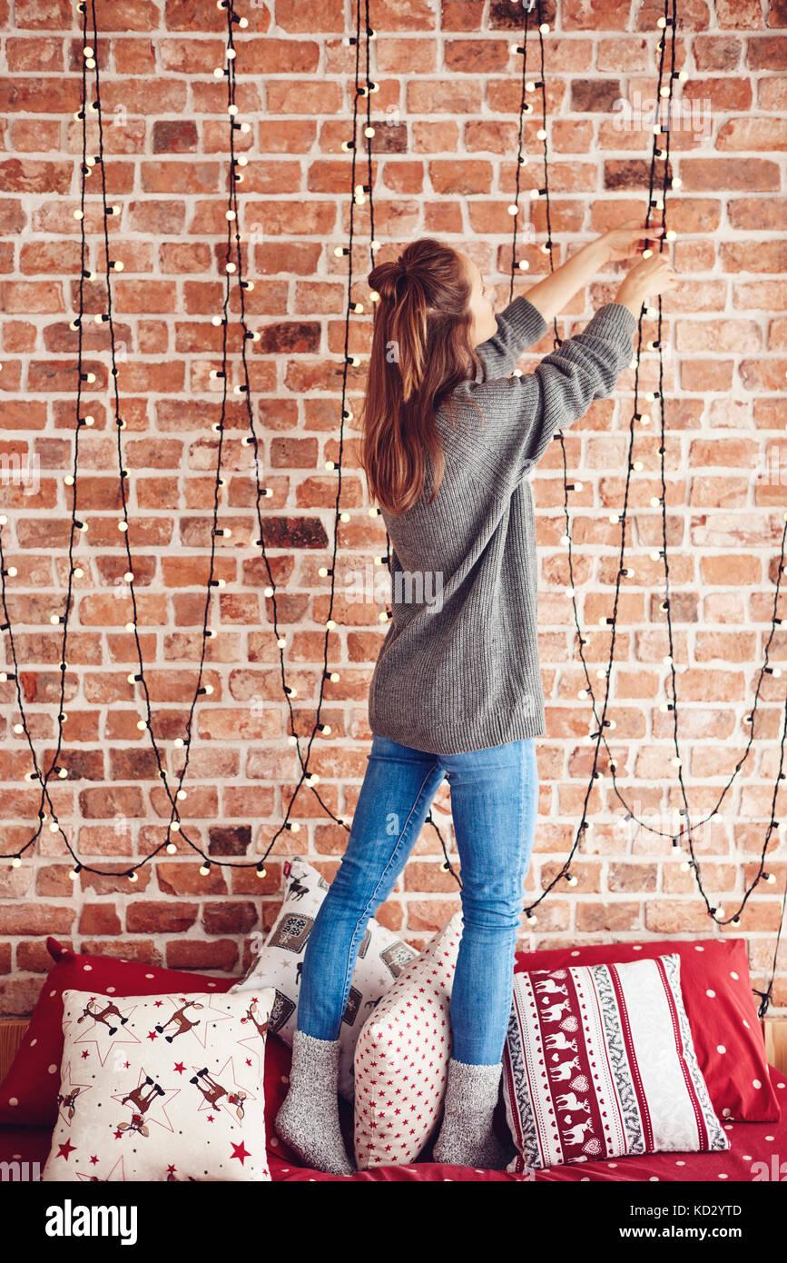 Woman standing on bed and hanging christmas lights Stock Photo