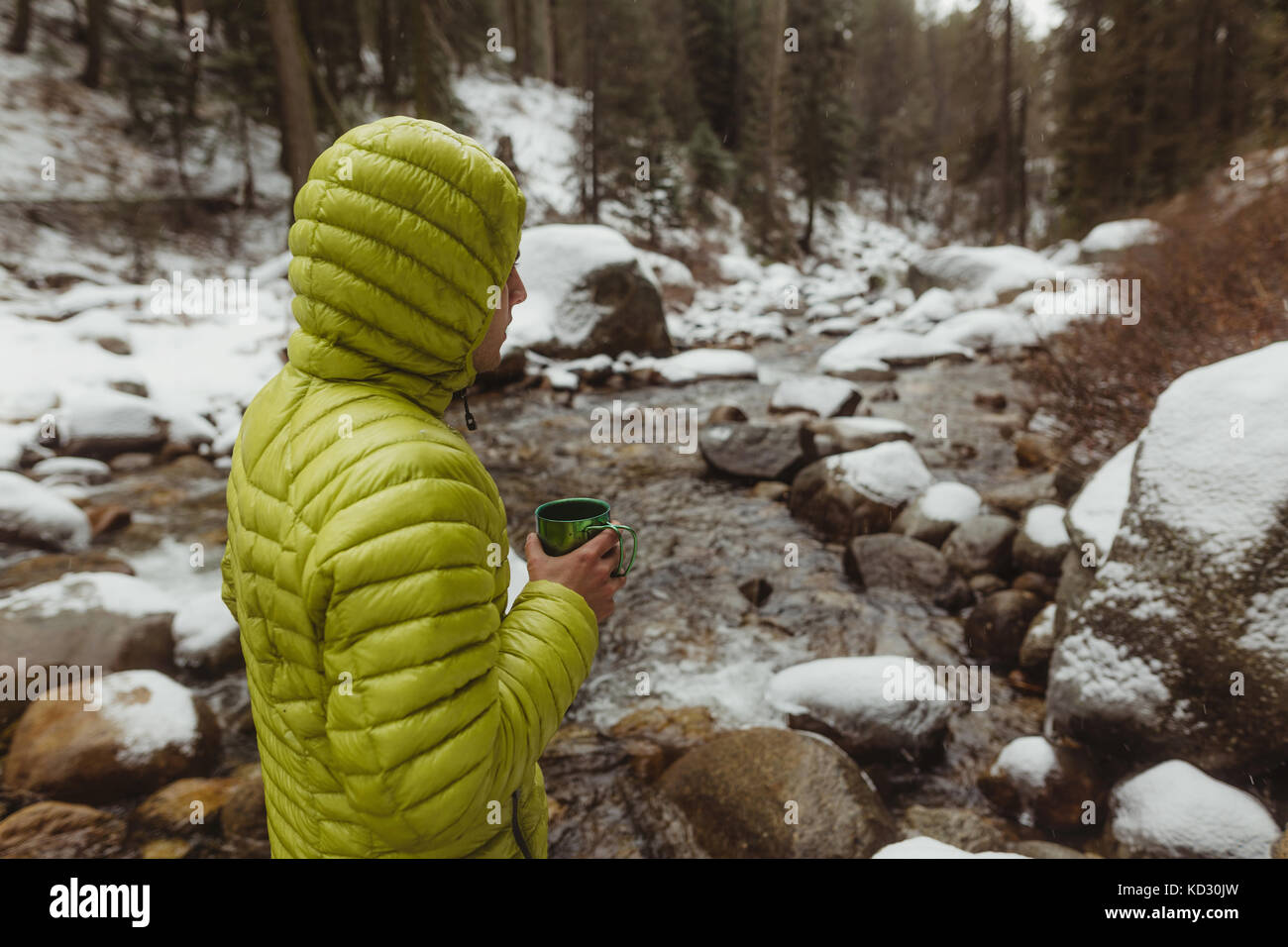 Young male hiker with coffee by snowy forest river, Sequoia National Park, California, USA Stock Photo
