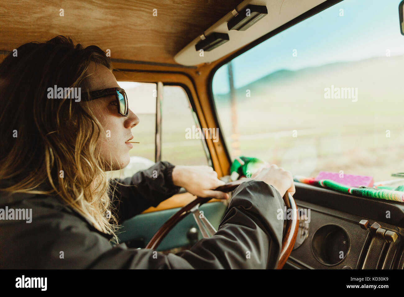Long haired young man in shades driving vintage vehicle Stock Photo