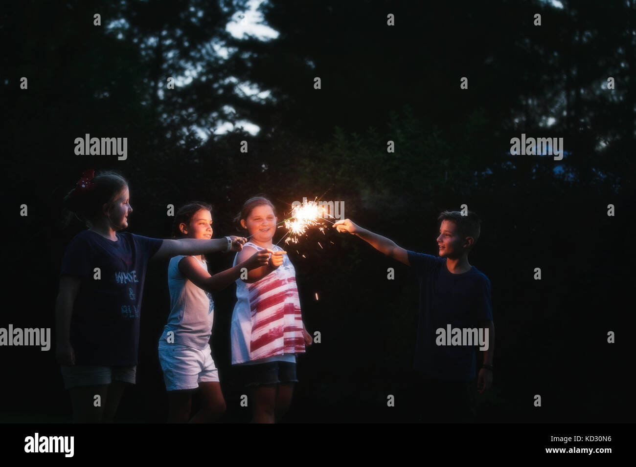 Boy and three girls igniting sparklers together at night on independence day, USA Stock Photo