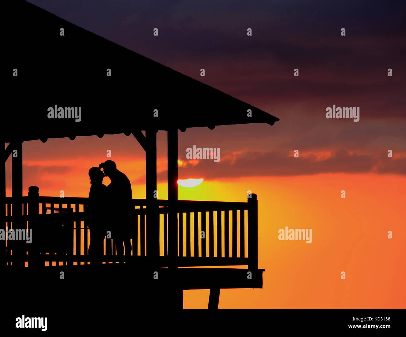 Lovers silhouetted against the sunset on a deck steals a romantic kiss ...