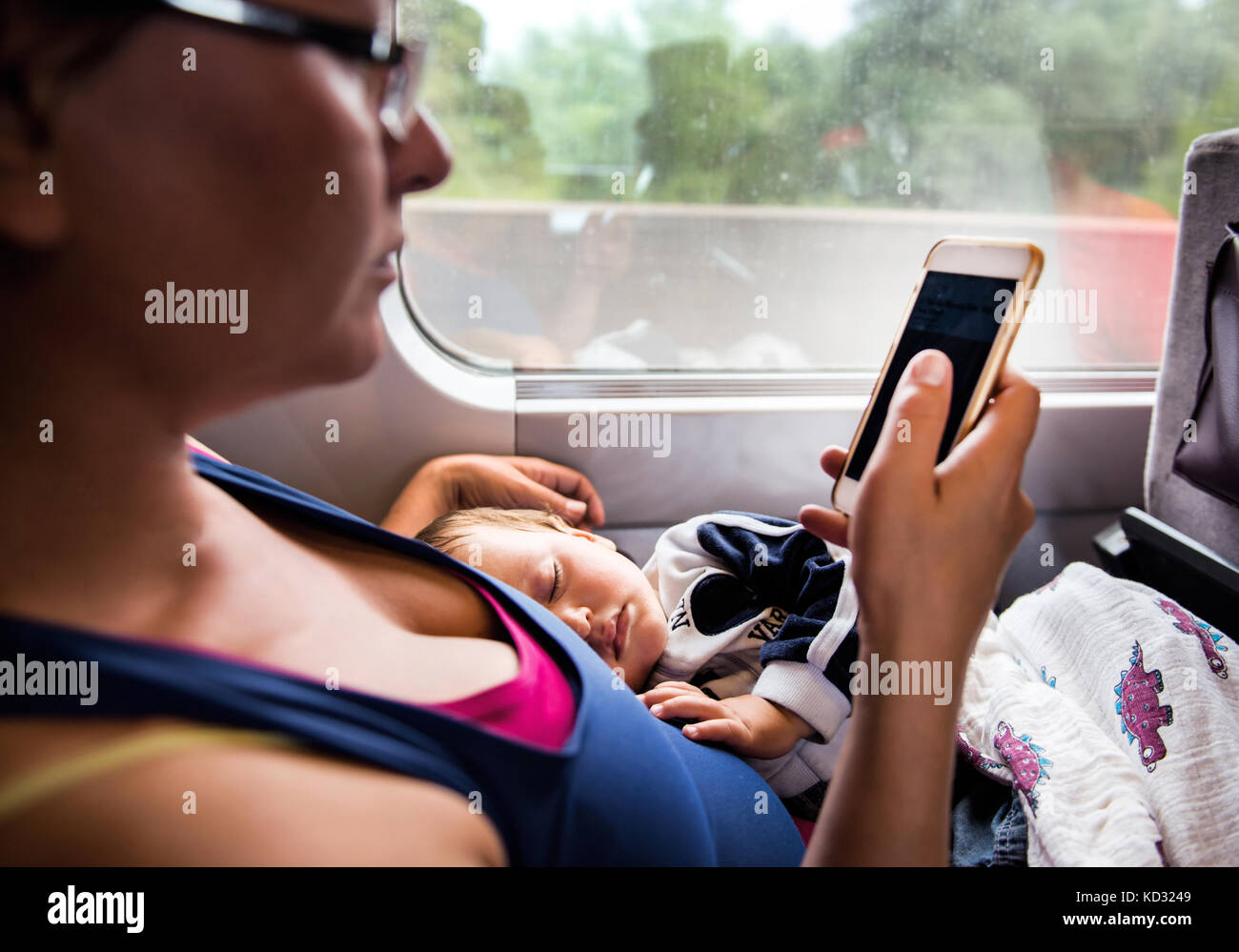 Mother and young son travelling on train, son sleeping, mother looking at smartphone Stock Photo