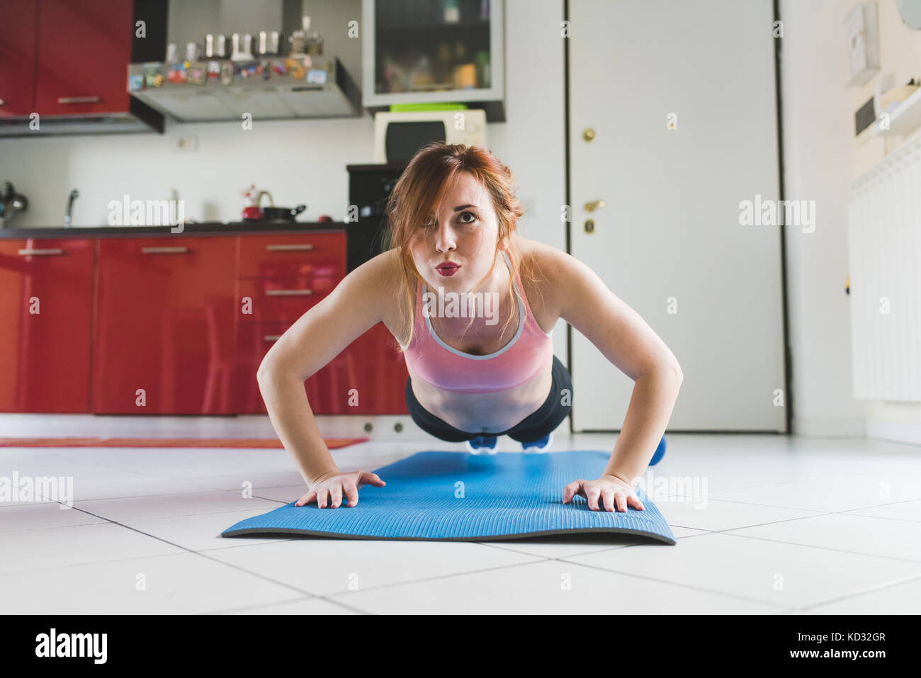 Portrait of young woman doing push ups on kitchen floor Stock Photo