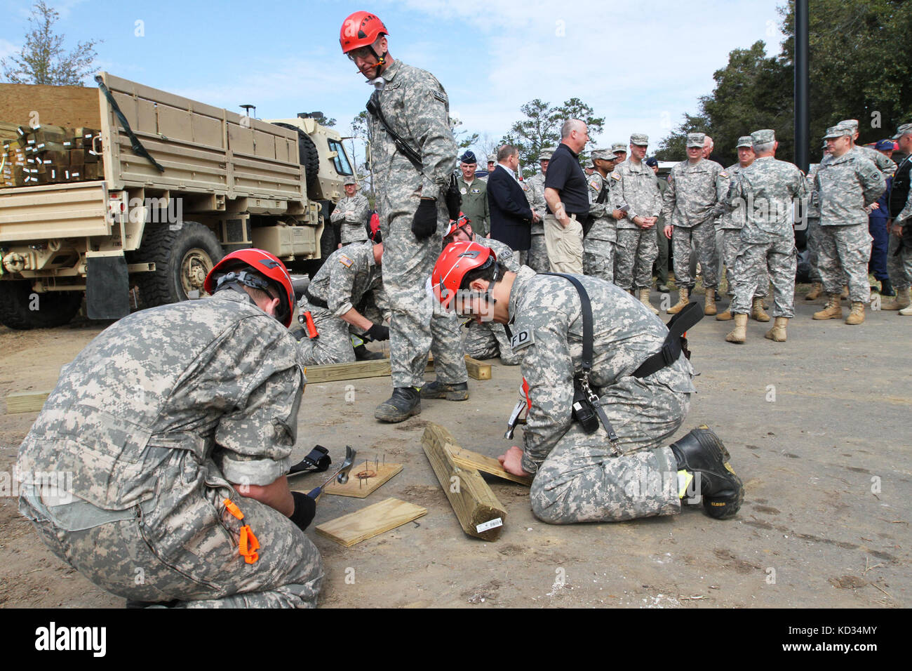 S.C. National Guard Soldiers from the 265th Engineer Detachment and 266th Fire Fighter Detachment hammer nails into boards that will be used to create supports to shore up the walls and roof of a building damaged for the training exercise, March 9, 2015, as Gen. Frank J. Grass, Chief, National Guard Bureau, Maj. Gen. Robert E. Livingston, Jr., Adjutant General for South Carolina and other dignitaries look on at Choppee Regional Resource Center (CRRC) in Georgetown, S.C. The training was part of Vigilant Guard 15, a training exercise consisting of National Guard Soldiers from South Carolina and Stock Photo