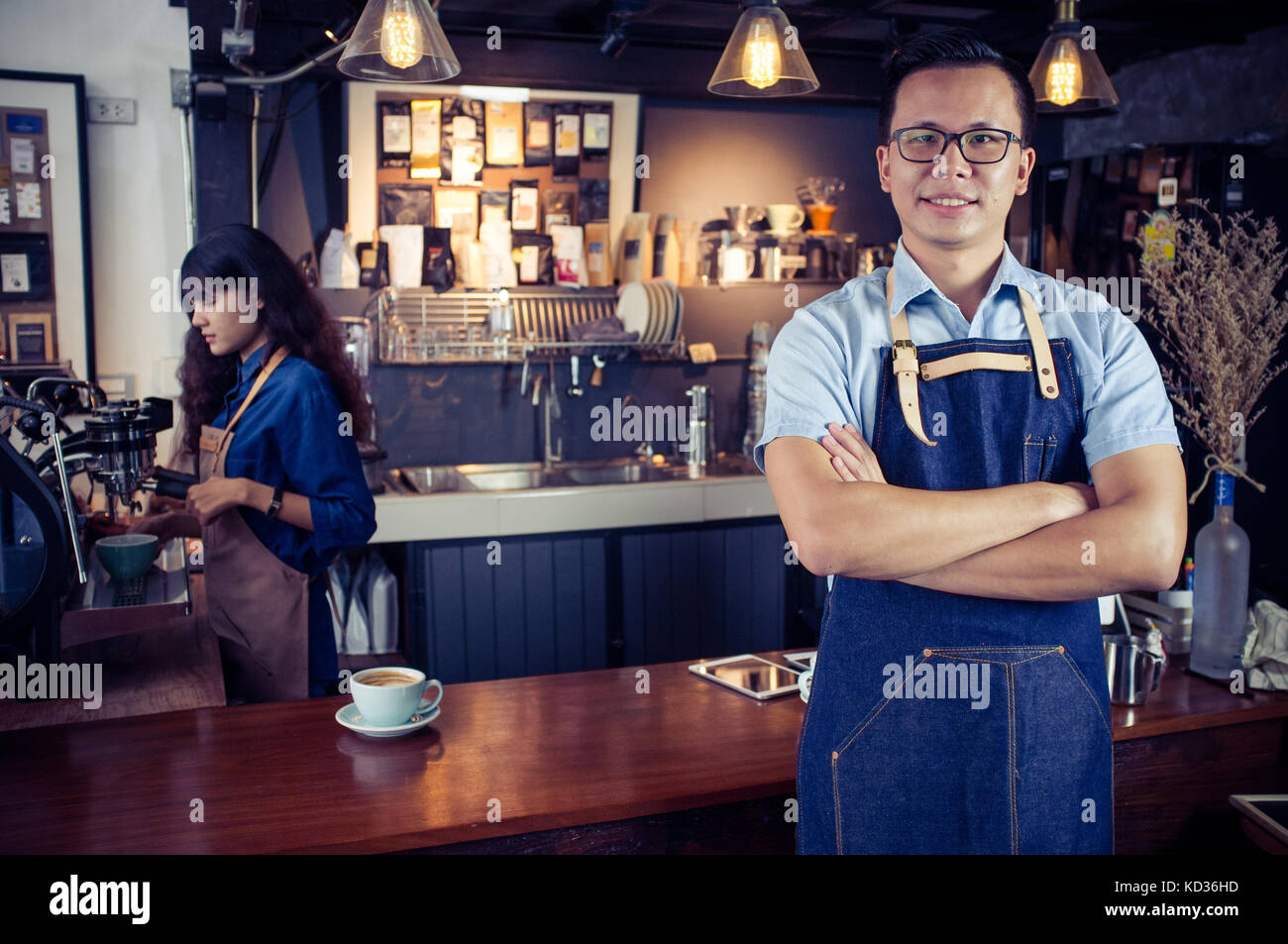 Portrait of smiling asian barista with arms crossed at counter in coffee shop. Cafe restaurant service, Small business owner, food and drink industry  Stock Photo