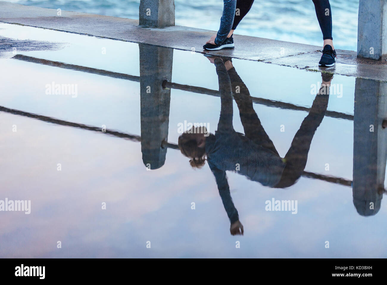 Exercising woman reflection in puddle of water on road. Fitness female