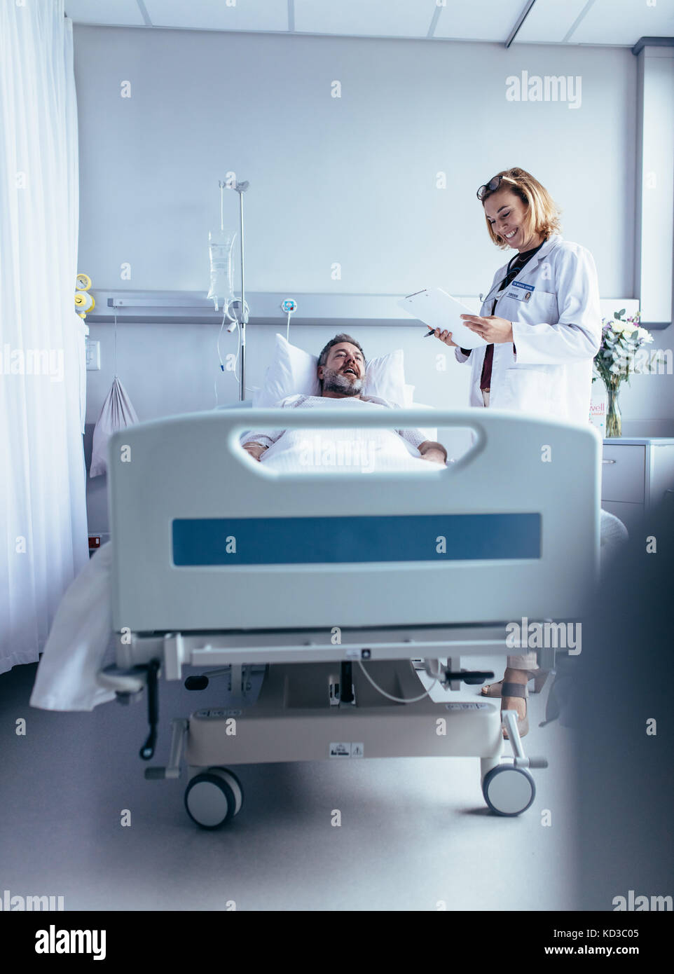 Smiling doctor with clipboard visiting man at hospital ward. Physician