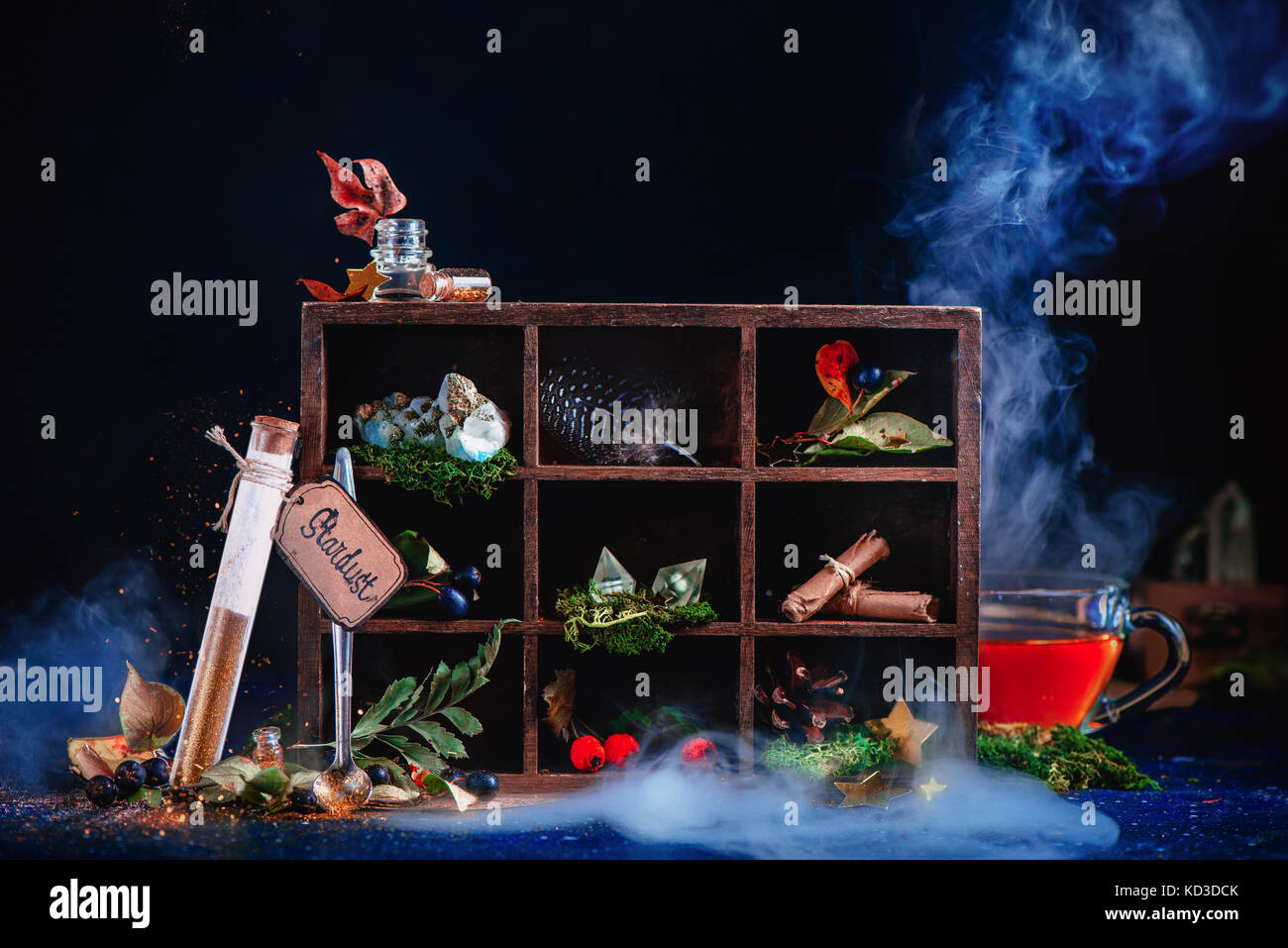Shining test tube with pixie dust. Steaming cup of tea in a magical still life with potion ingredients, berries, feather, scrolls, crystals and a wood Stock Photo
