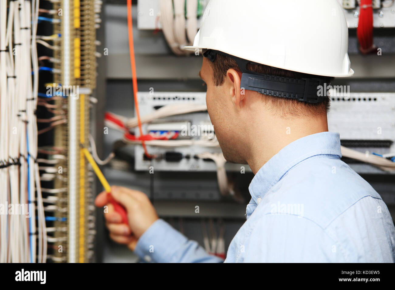 Engineer with screwdriver checking wire connections. Young electrician at work. Stock Photo