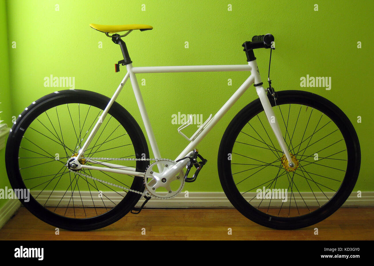 Single Speed steel frame bicycle leaning agains a bright green wall Stock Photo