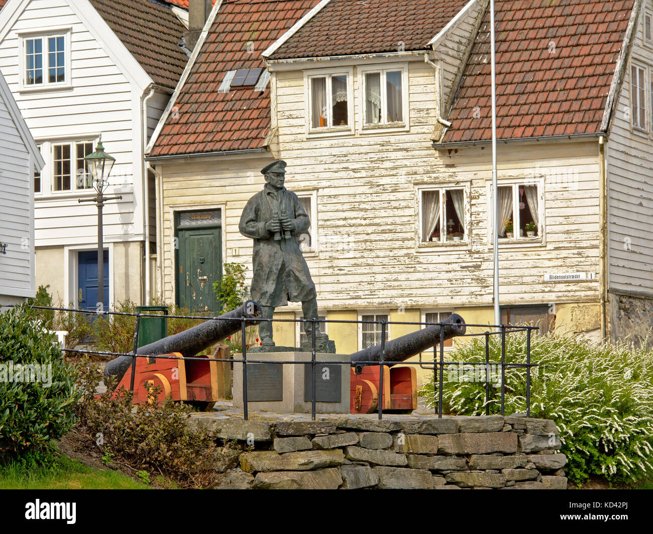 Bronze Statue to Admiral Thore Horve, leader of the Nrwegian Navy in the second world war, and canons in front of traditional white houses Stock Photo