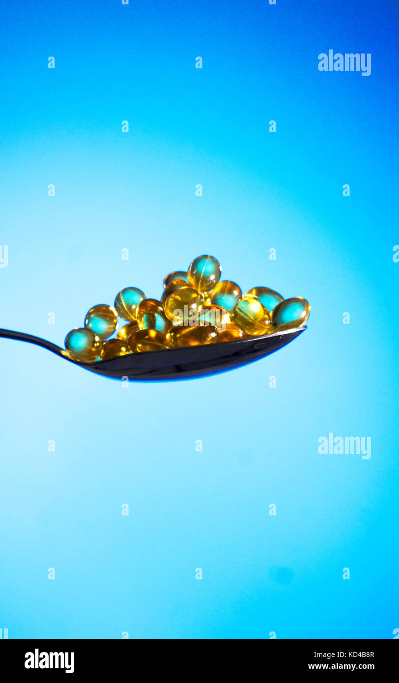 Fish oil pills with spoon back lit light blue background Stock Photo
