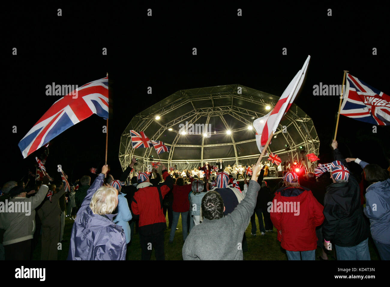 People waving the Union Jack flag at night in front of an illuminated dome stage. Stock Photo