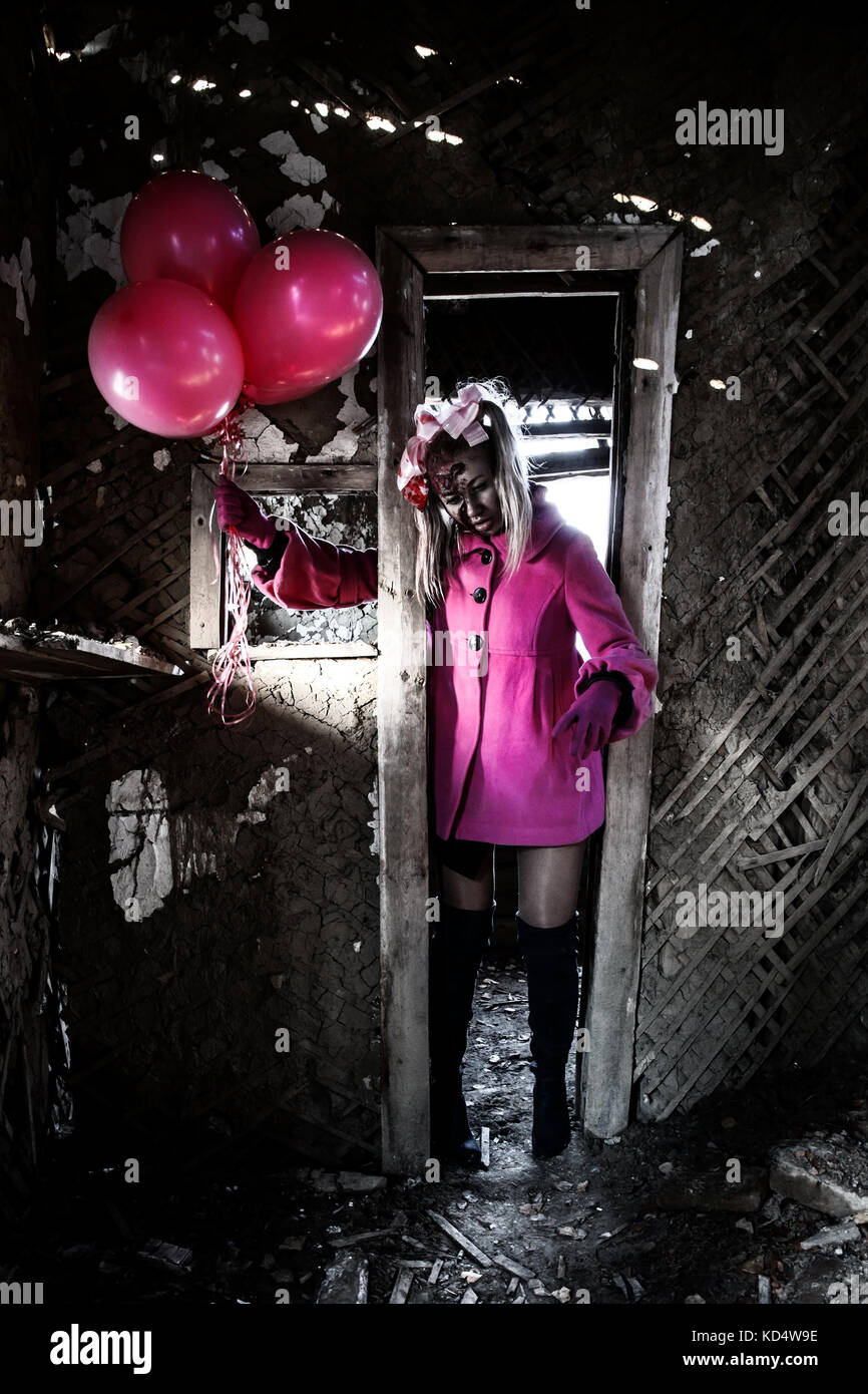 Zombie girl in a pretty pink coat walking through the broken door Stock Photo