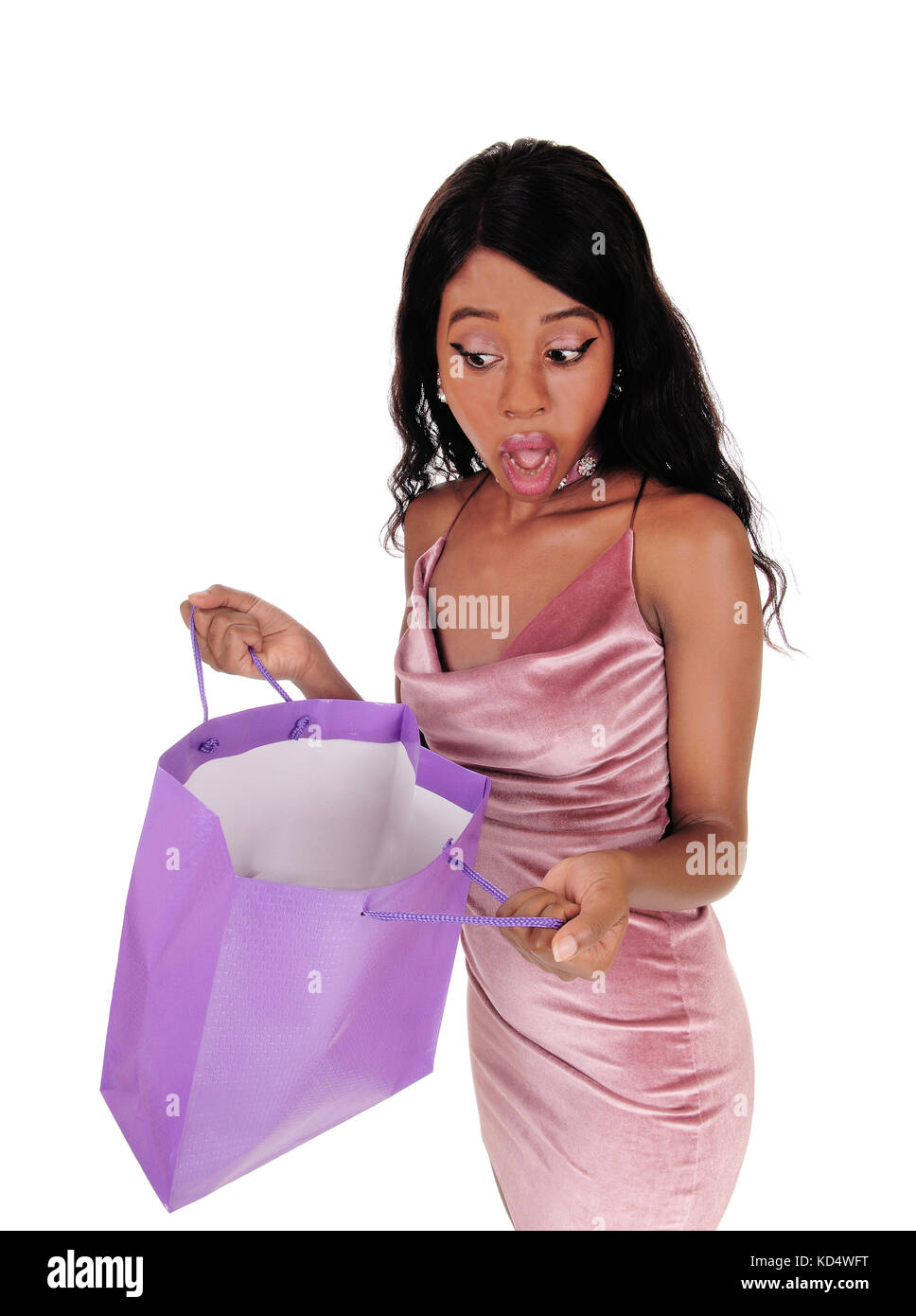 A shocked young African woman looking in her empty shopping bag standing in a pink dress, isolated for white background Stock Photo