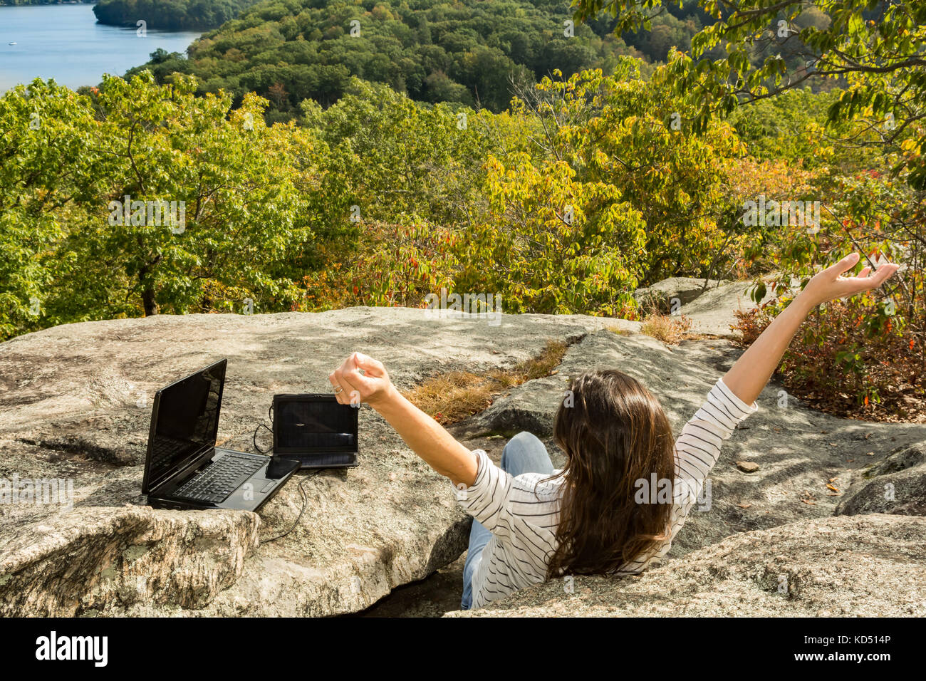 A woman charging her laptop with a solar panel at a remote work location. Stock Photo
