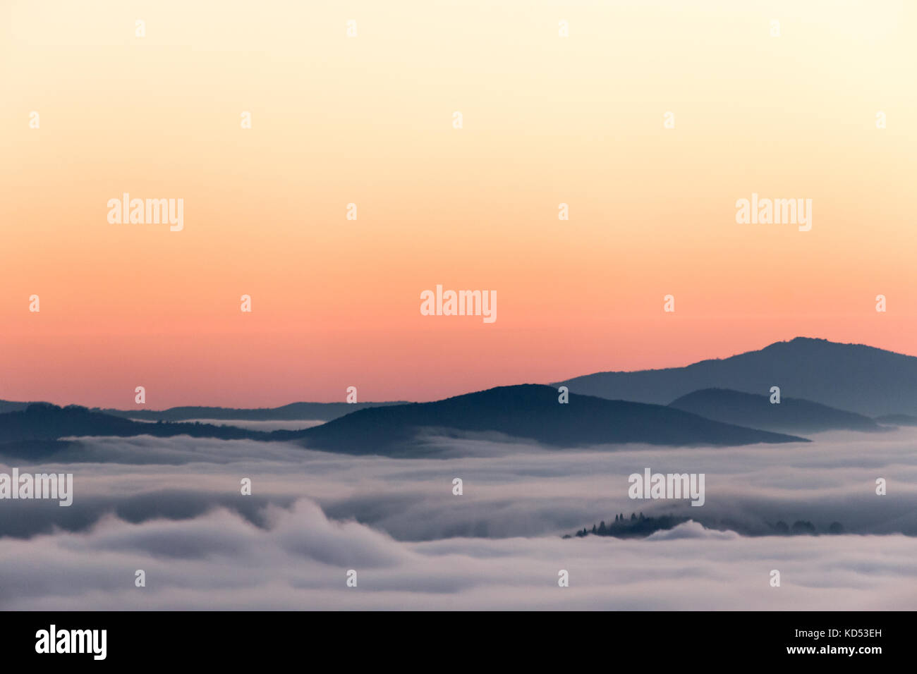 A valley filled by fog at sunset, with mist resembling sea with waves Stock Photo
