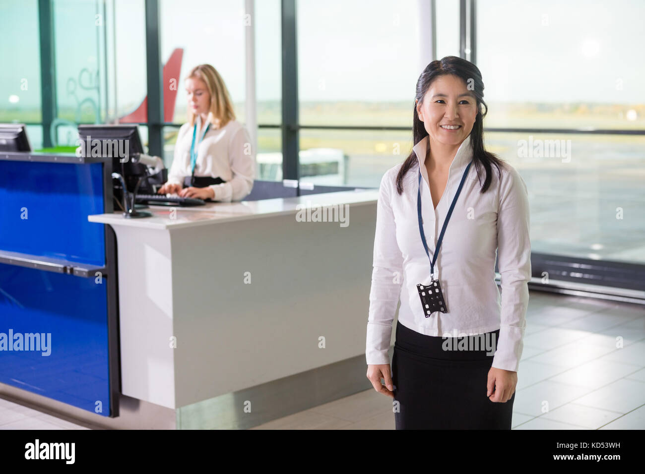 Mid adult ground staff looking away while colleague working at reception in airport Stock Photo