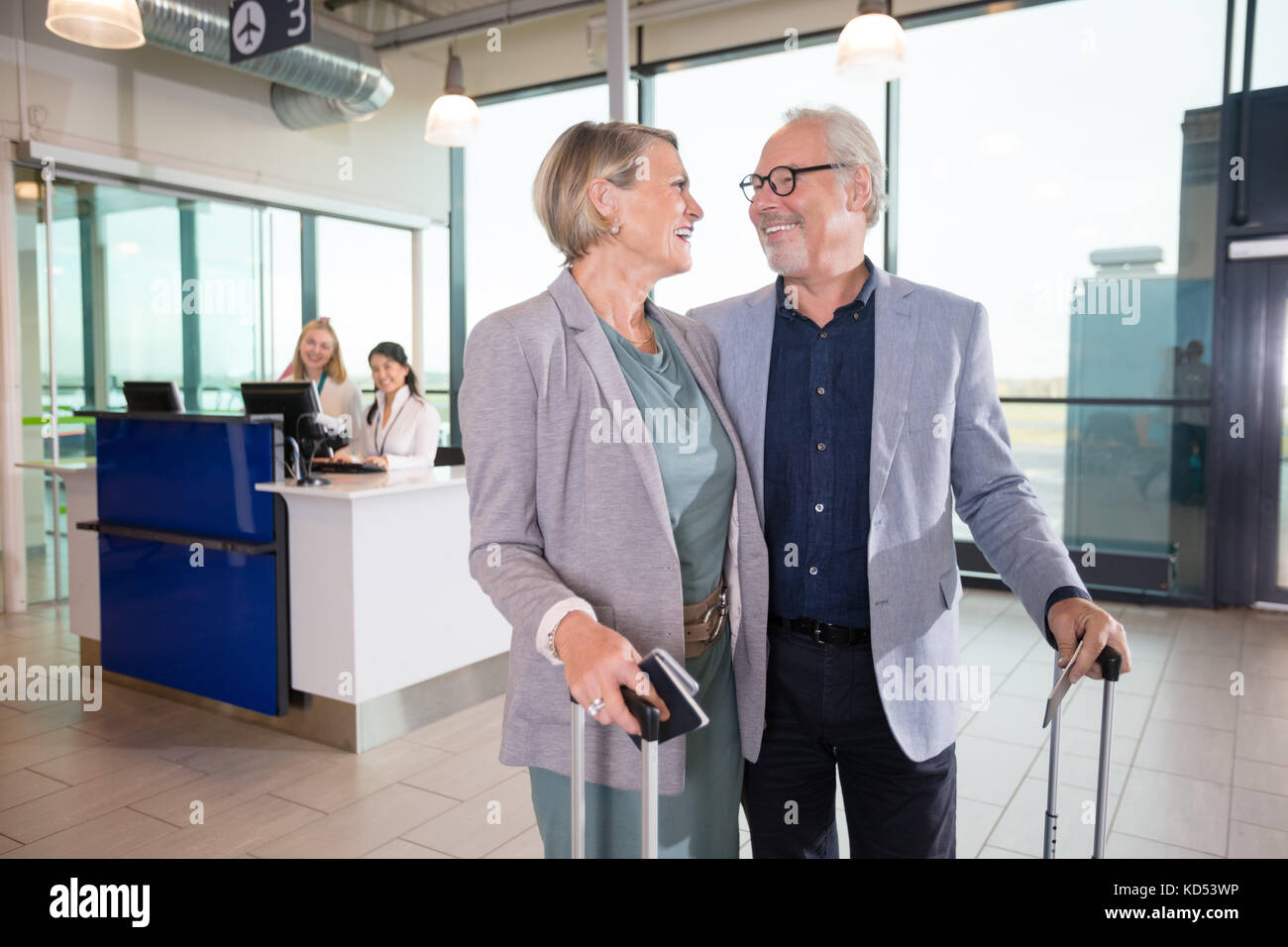 Happy senior business couple looking at each other with receptionists in background at airport Stock Photo