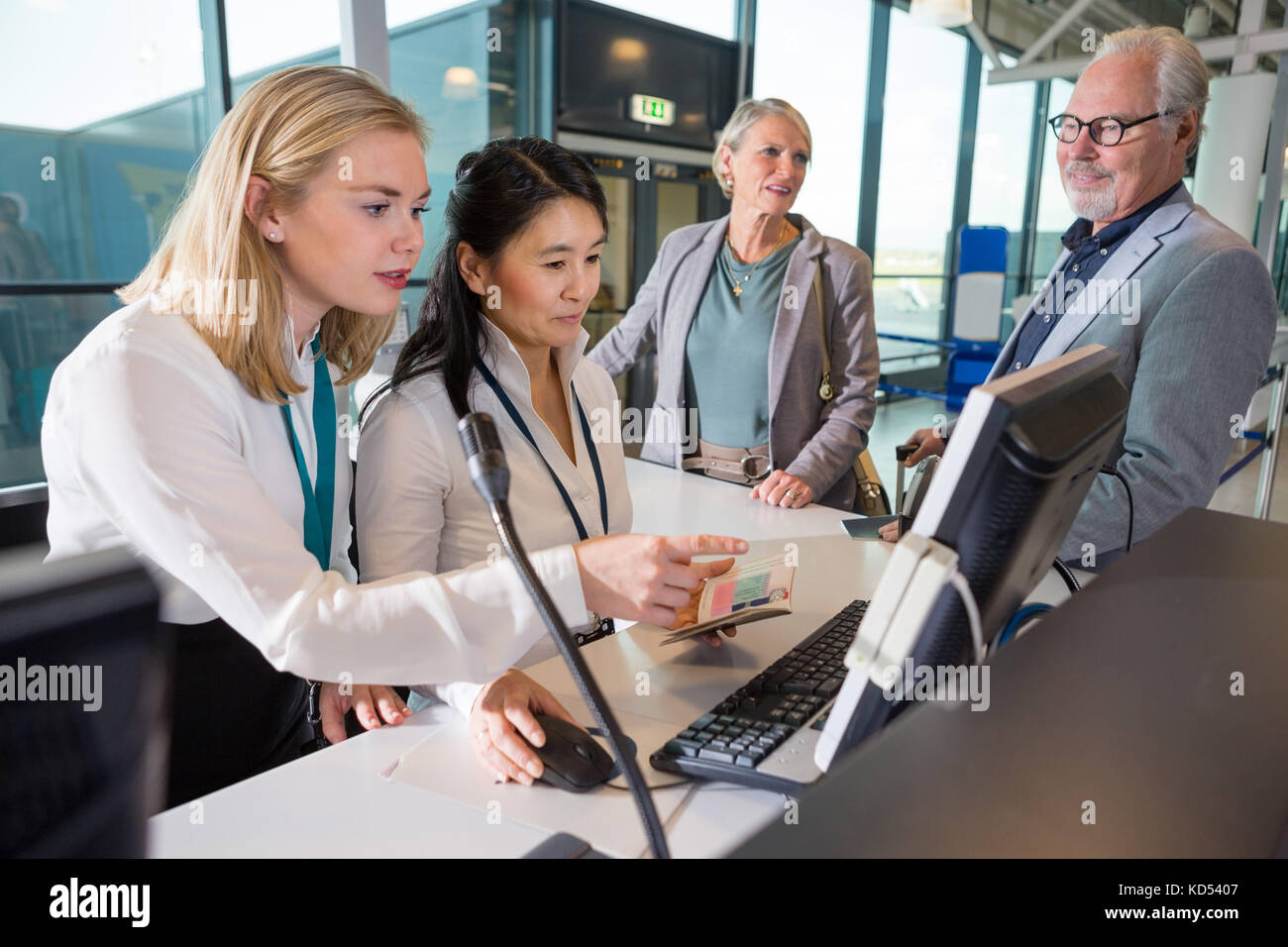 Mid adult female staff using computer together while passengers waiting in airport Stock Photo