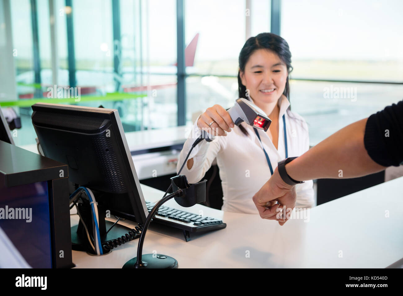 Smiling mid adult receptionist scanning smart watch of passenger at counter in airport Stock Photo