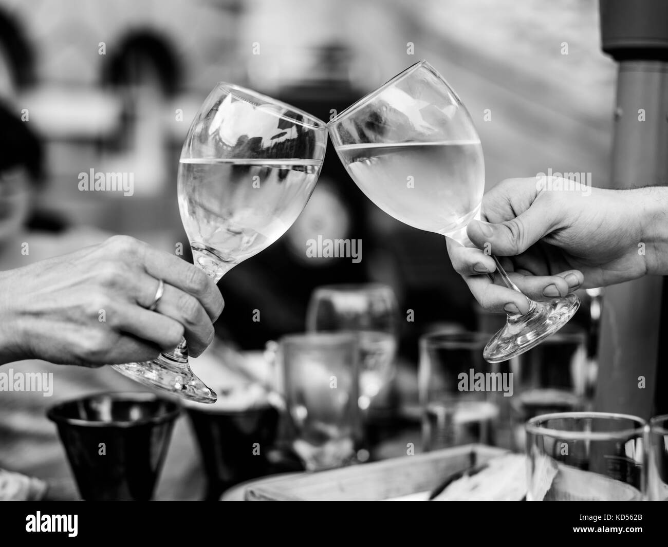 Black and White Monochrome Image of Celebrating Success With Two Raised Glasses of White Wine Across a Table In an Outside or Ourdoors Setting Stock Photo