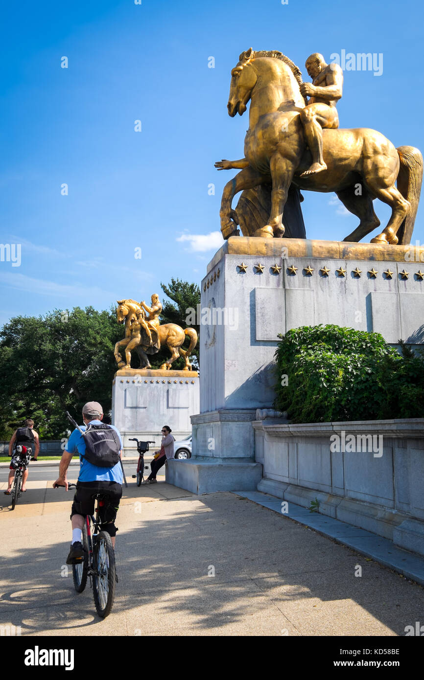 WASHINGTON DC-May 26, 2015: Bike riders approach the east entrance of the Arlington Bridge, under the gilded horse statues topping the bridge gates. O Stock Photo